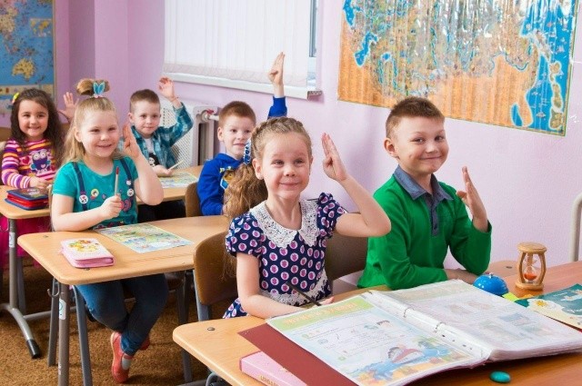 Дети за партами тянут руки, отвечая на занятии
